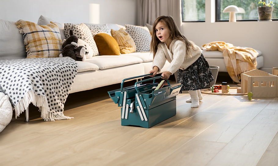 bambina che gioca con una cassetta degli attrezzi su un pavimento laminato beige in soggiorno